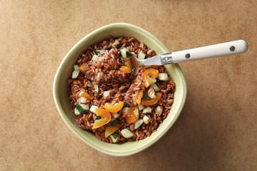 Bowl with tasty brown rice and vegetables on table