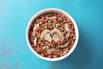 Bowl with tasty brown rice and mushrooms on color wooden background