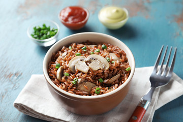 Bowl with tasty brown rice and mushrooms on color wooden table
