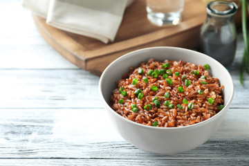Bowl with tasty brown rice on wooden table