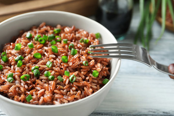 Bowl with tasty brown rice on table, closeup