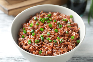 Bowl with tasty brown rice on table, closeup