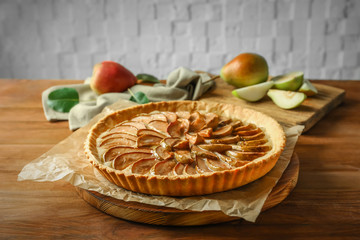 Wooden board with tasty pear tart on table