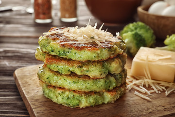 Wooden board with delicious broccoli pancakes on table, close up
