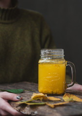 Female holding sea buckthorn tea in jar on wooden table