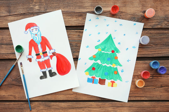 Child's paintings of Christmas tree with gifts and Santa Claus on wooden background