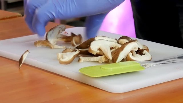 Slicing mushrooms for cooking on wooden tablein kitchen on cutting board. Chop fresh wild mushrooms. Hands with a knife cutting mushrooms. Man hand carefully cut mushrooms on kitchen's wooden board