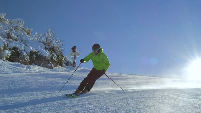 SLOW MOTION FOLLOW Alone happy skier enjoying vacation, skiing the first track on perfect groomed idyllic mountain ski piste in snowy winter at European ski resort. Sun is shining in background.