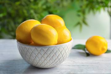 Bowl with ripe lemons on table against blurred background