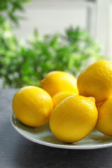 Plate with ripe lemons on table against blurred background