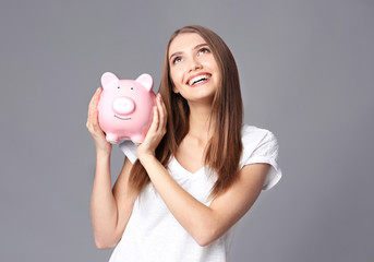 Beautiful young woman with piggy bank on grey background