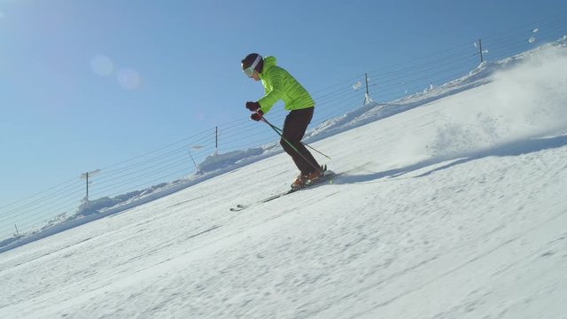 TRACKING SLOW MOTION: Pro skier wearing helmet skiing down a slope at sunny mountain ski resort on snowy winter day while morning sun is shining above the valley. Ski resort located in the Alps Europe