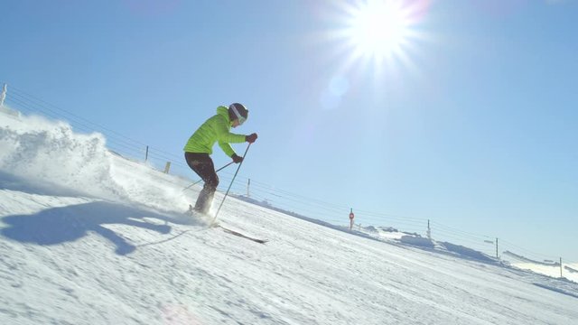 TRACKING SLOW MOTION: Amateur skier skiing for hobby down a slope at sunny mountain ski resort on snowy winter day while morning sun is shining above the valley. Ski resort located in the Alps, Europe