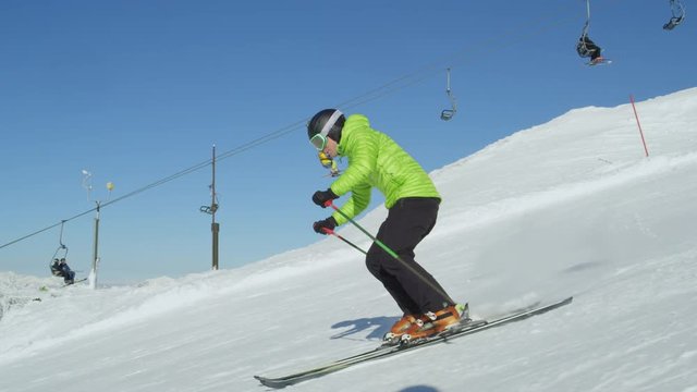 TRACKING SLOW MOTION Recreational skier enjoys idyllic perfect cold weather on a winter day for skiing down the groomed piste with ski lift in background. Ski resort located in the Alps, Europe.