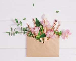 Decorative flat lay composition with makeup products, kraft envelope and flowers. Flat lay, top view on white background