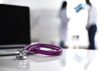 Laptop and stethoscope on the desk , doctors standing in the background