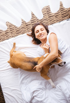 Woman plays with her beagle dog in bed in morning time