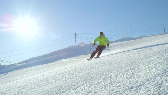 SLOW MOTION CLOSE UP: Recreational skier enjoys idyllic perfect weather in cold winter. Skiing alone on perfectly groomed ski piste with fresh snow at ski resort. Located on top of the mountain.
