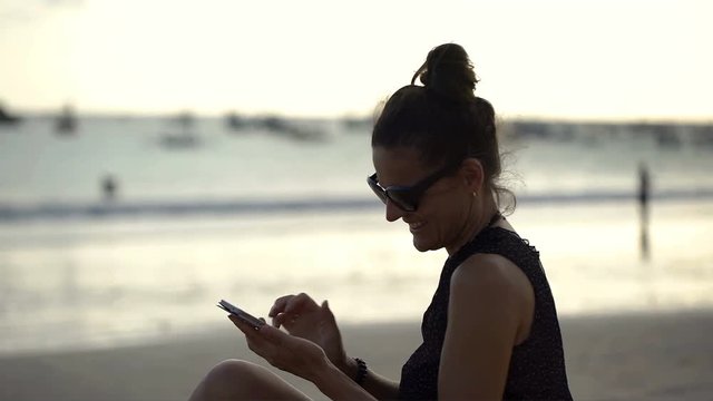 Beautiful woman relaxing on the beach and doing selfies on smartphone, steadycam shot
