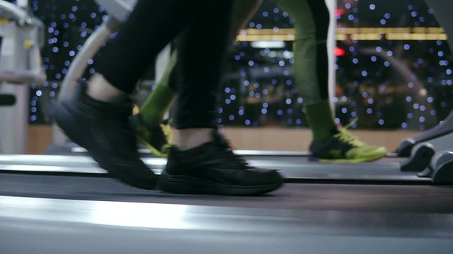 Side closeup view of a feet of a unrecognizable sportpeople in motion walking on treadmills in the gym warming up before training. Slowmotion shot