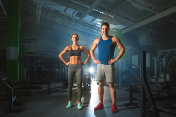 Fototapeta na wymiar The sport couple stand in the modern gym on the bright light background