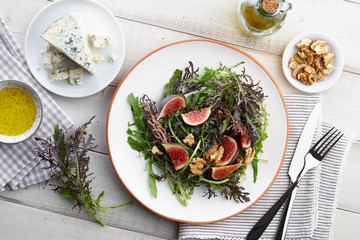 Salad with figs, blue cheese, arugula, mizuna and walnuts on white wooden background, top view