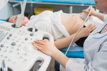 Doctor using ultrasound and screening stomach of pregnant woman.