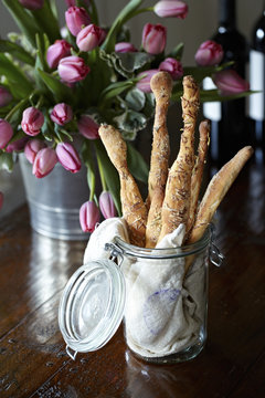 Handmade breadsticks in a jar on a dark table with tulips and wine