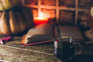 A cup of coffee in cozy rustic autumn atmosphere with the candles and a book