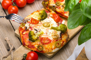 Tasty Italian homemade mini pizzas with broccoli, feta and olives served on wooden cutting board.