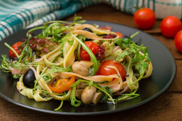 Italian bucatini with shrimp, arugula and cherry tomatoes. Wooden background. Close-up. Top view