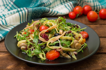 Italian bucatini with shrimp, arugula and cherry tomatoes. Wooden background. Close-up. Top view