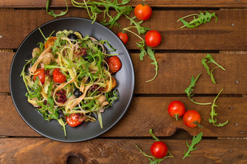 Italian bucatini with shrimp, arugula and cherry tomatoes. Wooden background. Close-up. Top view