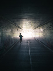 Woman running through tunnel towards bright light - 176023514