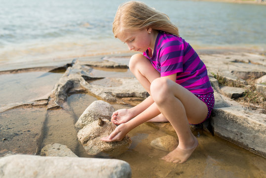 Little Girl Pretending to Kiss Frog on a Rocky Northern Cottage Lakeshore on Warm Sunny Summer Day