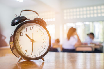 Closeup of Retro alarm clock with ten o'clock on table teacher in blur students exams classroom....