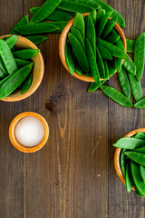 Fresh pea pods in bowls on dark wooden background top view copyspace