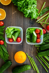Healthy meal in containers. Salad with tomato, cucumber, orange in containers on wooden background top view