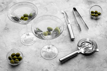 Make martini cocktails. Glass with beverage, olives and utensils on grey stone background top view