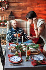Beautiful young couple cover the table in preparation for Christmas dinner in the beautifully decorated New Year interior with Christmas tree