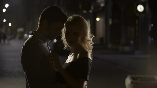 Blond female teasing and cuddling boyfriend in the night street, silhouettes