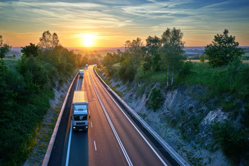 Three white trucks driving on the highway in a rural landscape at sunset. View from above.