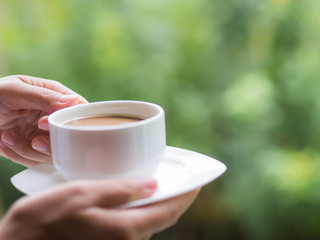Woman hand holding a cup of coffee at the gaerden in the morning, with selective focus. Relaxing and healthy concept.