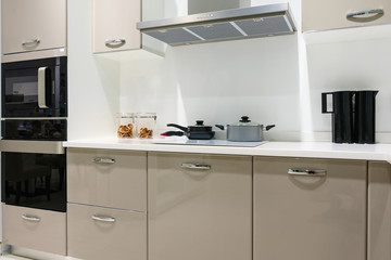 Modern kitchen furniture with contemporary kitchenware like hood, black induction stove and oven in house.