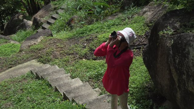 Young girl walks through tropical park and takes pictures of the beauty of nature stock footage video