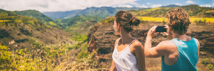 Couple tourists taking phone pictures of Hawaii nature landscape with smartphone camera app. Travel lifestyle people enjoying summer vacation.