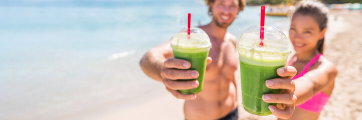 Fitness couple drinking green smoothie at beach banner panoramic. Man and woman holding vegetable smoothies after running sport fitness training. Healthy clean eating lifestyle concept.