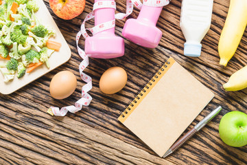 Healthy eating, dieting, slimming and weight loss concept - Top view of green apple, bananas, measuring tape, dumbbells, blank note book and vegetables on wooden background. copy space for Text
