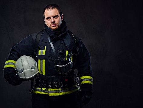 Firefighter dressed in uniform holds safety helmet.