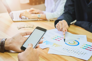 The man holds the phone on a wooden desk in the office. The members are currently meeting. Technological concepts make progress.